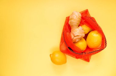Sarı arka planda sebze ve meyve paketlemek için kırmızı torbada taze limon ve zencefil kökü. Seçici odak.