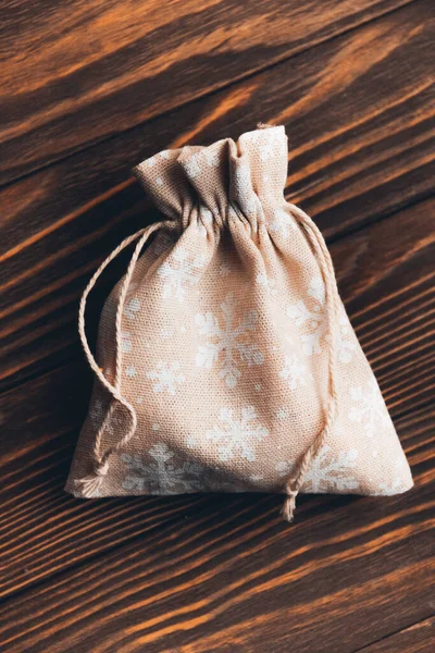 textile decorative handmade bag with the image of white snowflakes on a Christmas theme on a wooden background. Selective focus.