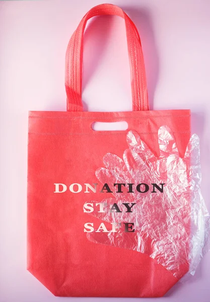 Red grocery bag and transparent protective gloves. Donation, stay safe. Concept of food delivery in a grocery bag with protective gloves, security measures, selective focus.