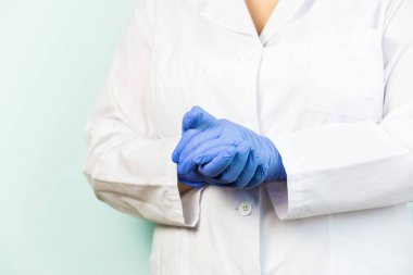 Beyaz üniformalı, mavi arka planda duran bir kadın tıbbi eldiven giyiyor. Seçici odak.