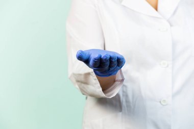 Uzamış eli olan tıp eldivenli bir kadın beyaz üniformalı mavi bir arka planda duruyor. Seçici odak.