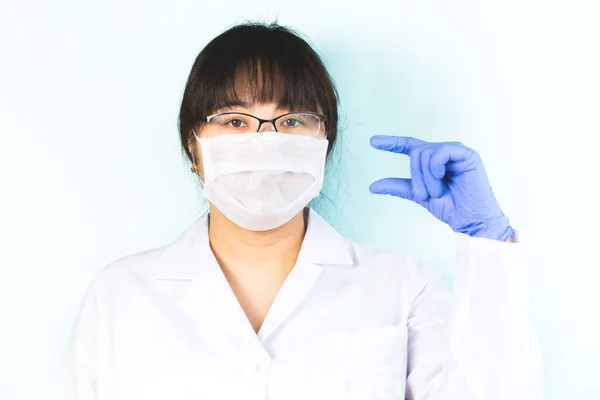 The woman wears a medical mask in a white uniform, protective blue, shows a small size of something. Selective focus.