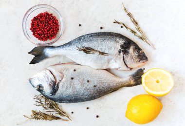 Pişirme malzemeleriyle birlikte beyaz bir masada taze çiğ Dorado balığı. Boşluğun bir kopyasına sahip üst görünüm, seçici odak.