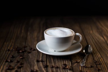 Süt ve köpüklü bir fincan kahve, koyu ahşap arka planda kahve çekirdekleri. seçici odak.