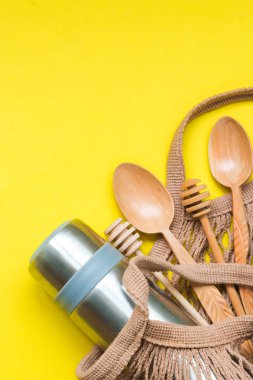 Tekrar kullanılabilir su şişeli kahverengi ağ torbası, sarı arka planda kaşıklar. Sürdürülebilir yaşam tarzı. Sıfır atık ve plastik kavram yok.