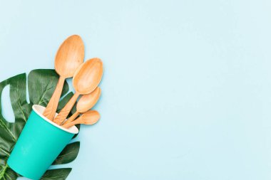 Kağıt bardakta ahşap kaşıklar ve mavi arka planda yeşil yaprak, üst manzara. Sıfır atık, çevre dostu kavram.