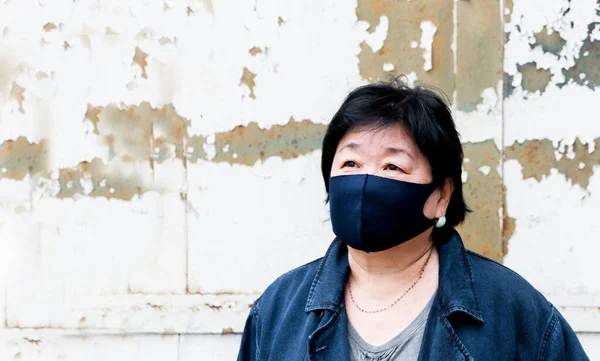 Protection of human face masks in a public place, prevention of coronavirus. Protection against the coronavirus pandemic, flu epidemic. An Asian woman aged about 65 years old in a mask poses.
