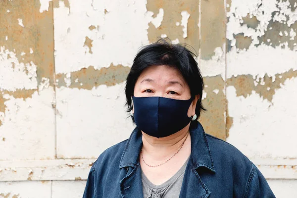 Protection of human face masks in a public place, prevention of coronavirus. Protection against the coronavirus pandemic, flu epidemic. An Asian woman aged about 65 years old in a mask poses.