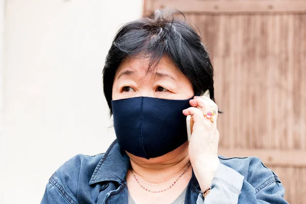 Protection of human face masks in a public place, prevention of coronavirus. Asian woman in a mask talking on a mobile phone.