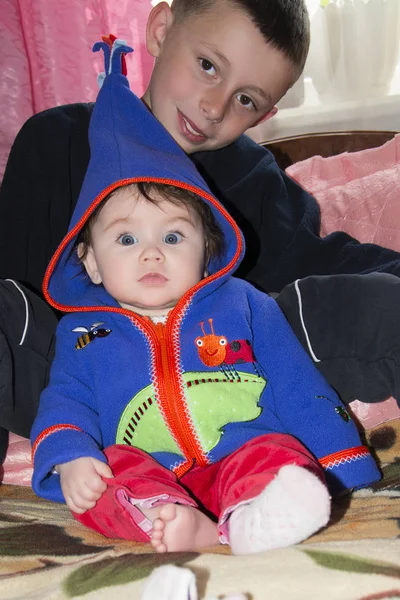 Little brother and sister are sitting on the bed in the room — Stock Photo, Image