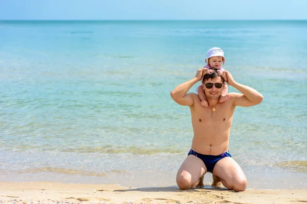 Jovem pai de óculos senta-se na praia com sua filha — Fotografia de Stock