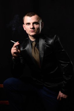Çekici bir genç adam bir takım elbise ve kravat siyah bir zemin üzerine bir sigara tutar.