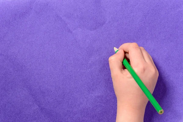 A mão de um menino pinta um lápis verde em um papel roxo — Fotografia de Stock