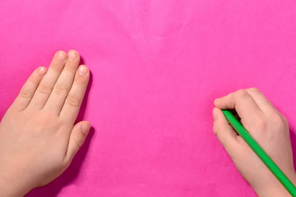 Dwie ręce małego chłopca, który farby zielony ołówek na tle różowy — Zdjęcie stockowe
