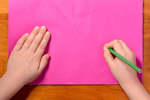 Дві руки маленького хлопчика, який малює зелений олівець на рожевому тлі — стокове фото