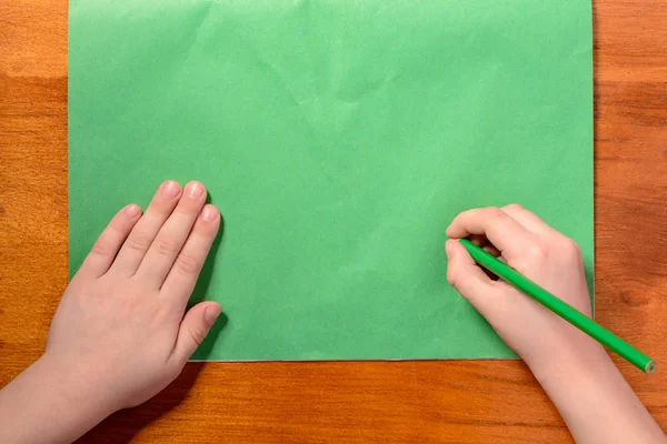 Las manos del niño sostienen un lápiz verde sobre el fondo de papel verde —  Fotos de Stock