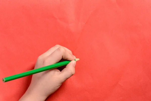 La mano de un niño sostiene un lápiz verde sobre un fondo rojo —  Fotos de Stock