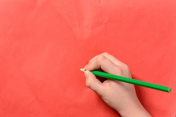 Рука хлопчика тримає зелений олівець на червоному тлі — стокове фото