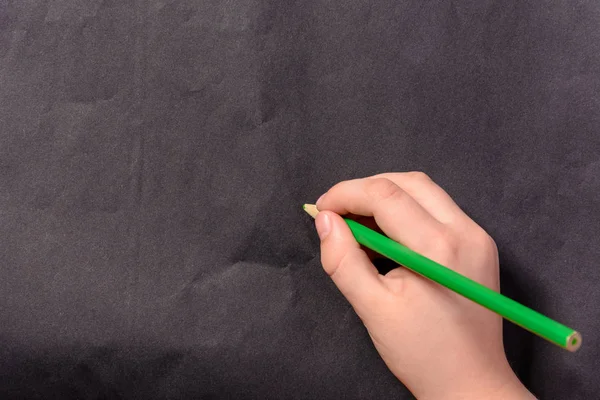 La mano de un niño escribe un lápiz sobre un fondo negro —  Fotos de Stock