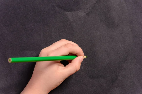 Ręka chłopca pisze ołówkiem na czarnym tle — Zdjęcie stockowe