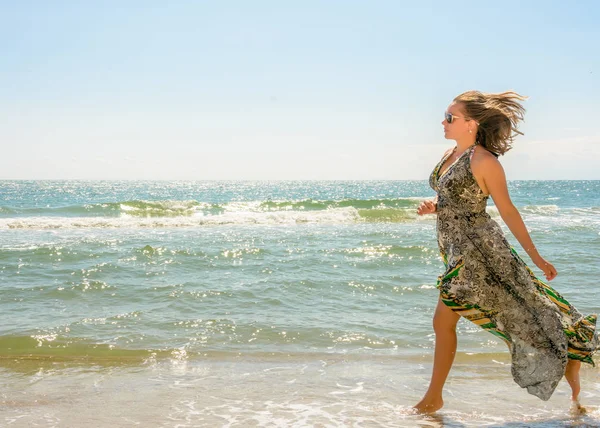 Une jolie femme courant le long d'une plage de mer noire dans une robe contre le ciel — Photo