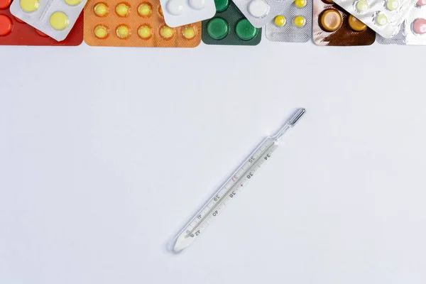 在包装上不同颜色的药丸之间的白色背景温度计 — 图库照片