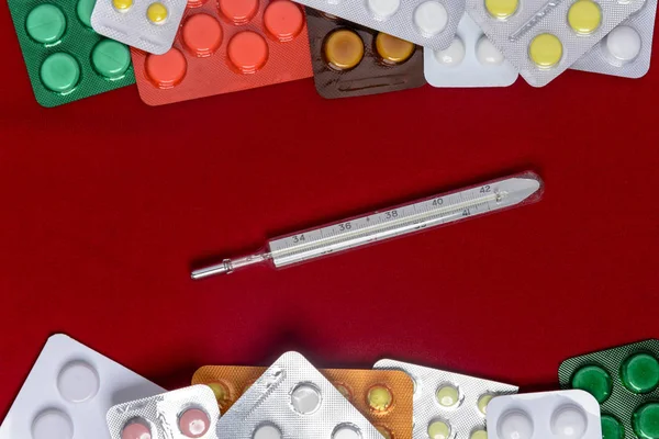 Thermometer with pills around and on a red background — Stock Photo, Image