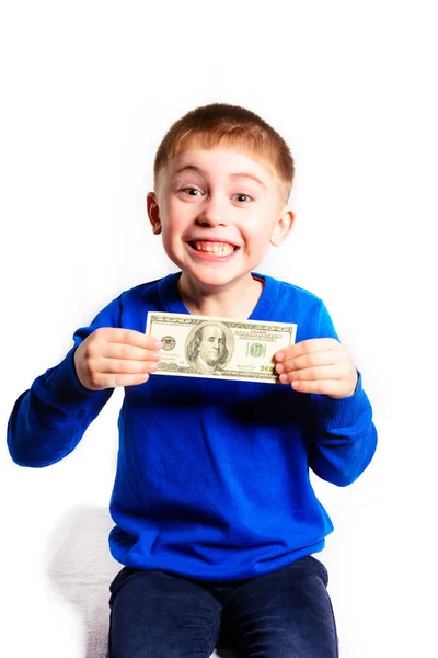 Маленький мальчик в синем свитере улыбается и держит в руках сто долларов — стоковое фото