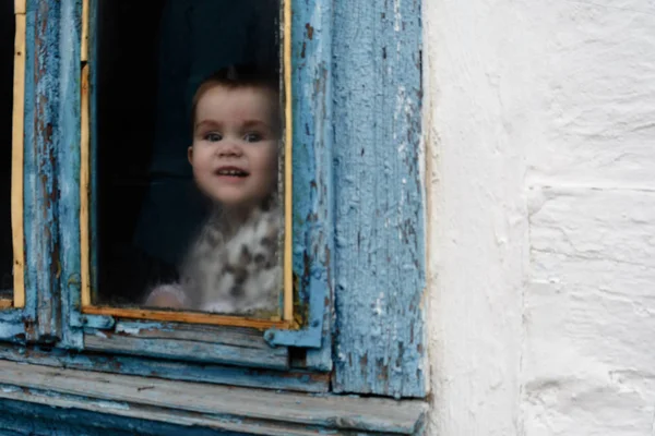 Uma menina senta-se em uma cabana velha em uma janela em que a pintura desapareceu — Fotografia de Stock