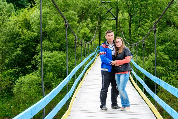 Молодые влюбленные стоят на мосту через реку возле зеленых деревьев — стоковое фото