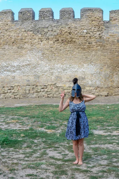 要塞の壁の近くの彼女の頭の上のヘルメットのドレスを着た少女 — ストック写真