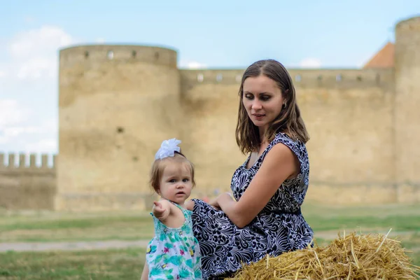 Eine junge Mutter mit ihrer Tochter sitzt auf einem Strohhalm in der Nähe der Festung — Stockfoto