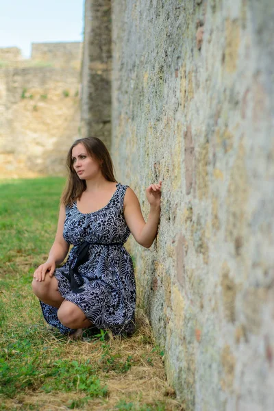 Όμορφο κορίτσι σε ένα φόρεμα κάθεται στο παρασκήνιο του τείχους του φρουρίου — Φωτογραφία Αρχείου
