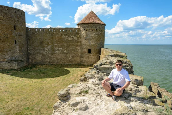 Giovane in occhiali da sole siede sulla parete della fortezza in riva al mare — Foto Stock