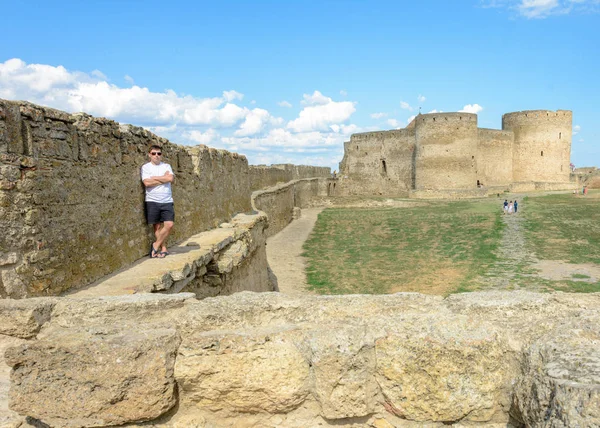 Un jeune homme en T-shirt blanc et lunettes de soleil se tient sur le mur de la forteresse — Photo