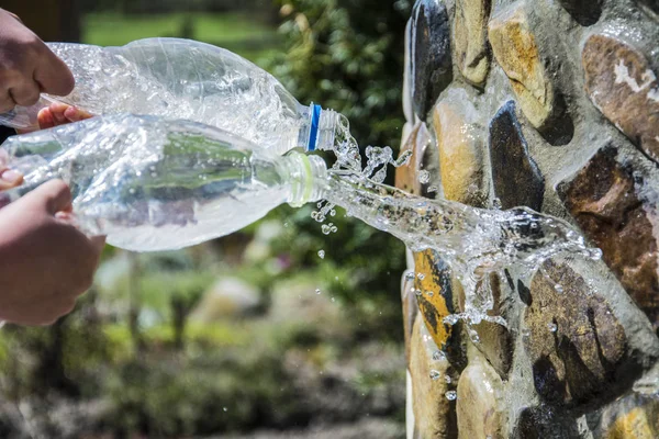 Hands hold a bottle of water and under pressure, sprinkle with a jet of the yard — Stock Photo, Image