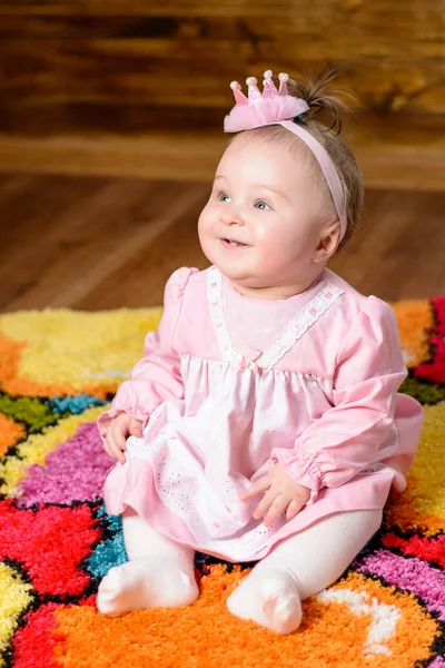 Pequena menina bonita em um vestido rosa ri em uma cama de bebê — Fotografia de Stock