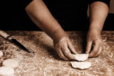 Yaşlı bir kadın üst üste bir tabloda koyu arka plan üzerinde köfte yapar