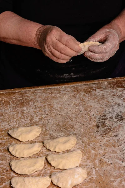 Le mani di una vecchia nonna modellano vareniks su uno sfondo scuro — Foto Stock