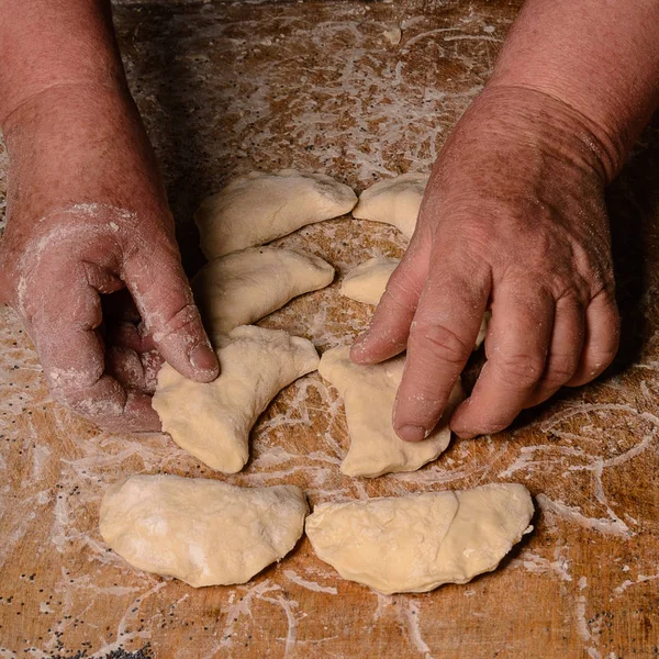 Una vecchia signora fa gnocchi di fila su un tavolo su uno sfondo scuro — Foto Stock