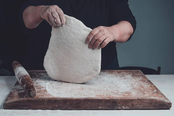 Egy nő ráncos kezében tartsa a kiolvasztott tésztát egy sötét háttér — Stock Fotó