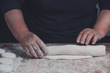 Yaşlı bir kadın karanlık bir arka plan üzerinde pişirme için ham bir meyilli dışarı rulo