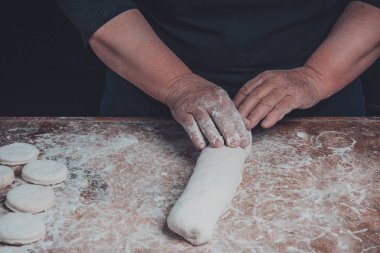 Yaşlı bir kadın karanlık bir arka plan üzerinde pişirme için ham bir meyilli dışarı rulo