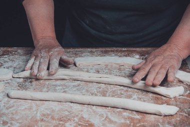 Yaşlı bir kadın karanlık bir arka plan üzerinde pişirme için ham bir meyilli dışarı rulo