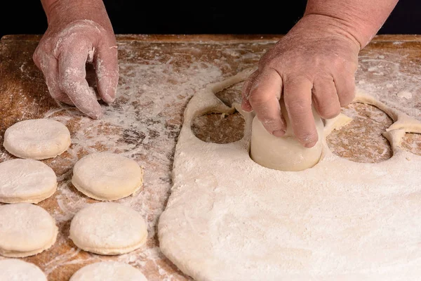 Granny squeezes a glass of a circle in a dough on the table