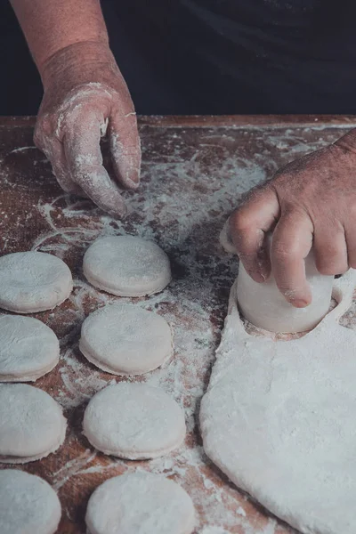 Granny squeezes a glass of a circle in a dough on the table