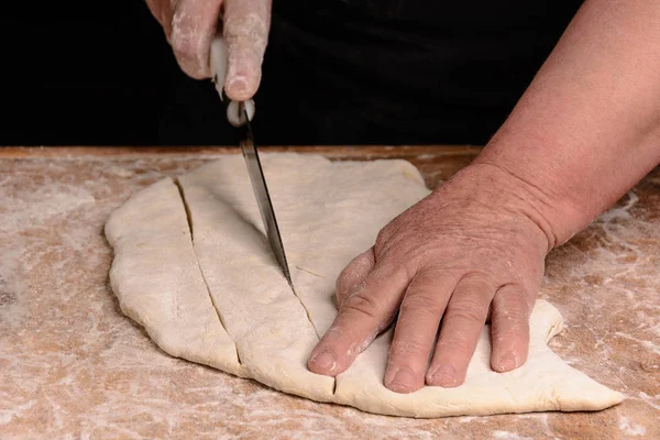 El cocinero corta masa cruda con un cuchillo en una línea estrecha —  Fotos de Stock