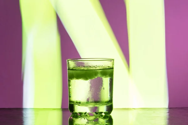Vloeistof met ijs in een glas op een reflecterend oppervlak op een rode achtergrond — Stockfoto