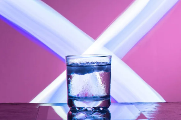 Vloeistof met ijs in een glas op een reflecterend oppervlak op een rode achtergrond — Stockfoto