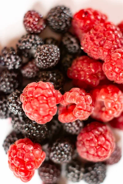 Bayas frescas de frambuesas rojas y negras dulces sobre un fondo blanco . —  Fotos de Stock